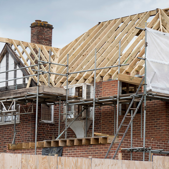 Roof construction with wooden framework and scaffolding on brick house undergoing renovation featuring two levels of scaffolding and cloudy sky