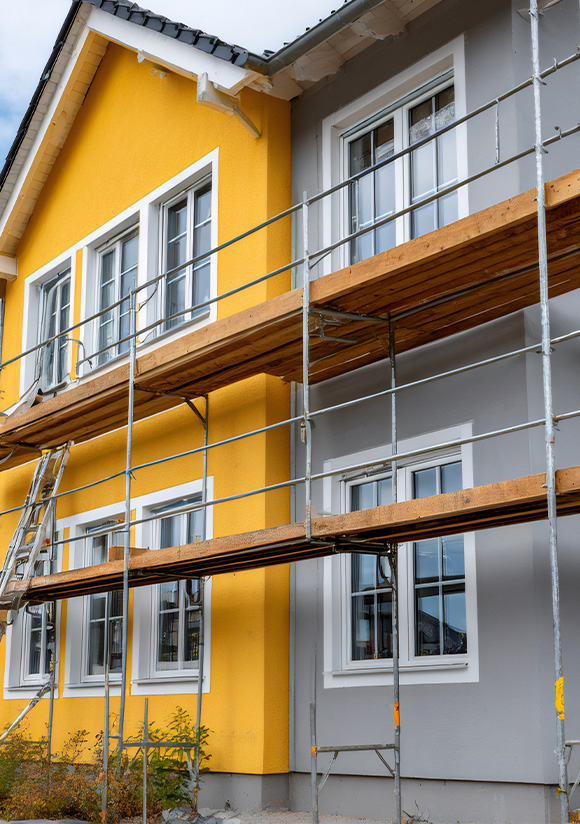 a spacious modern living room featuring a large sectional couch with colorful pillows a round wooden coffee table and large windows providing natural light with a view of greenery and a dining area in the background relaxing space for gatherings